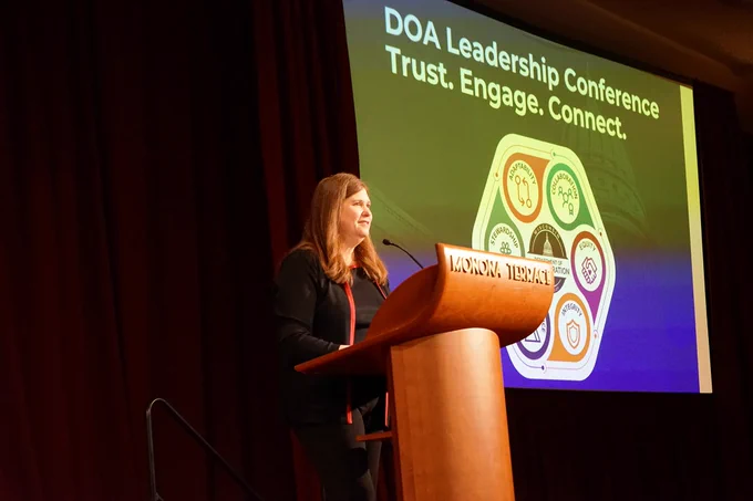 DOA Secretary Kathy Blumenfeld addresses the DOA Winter Leadership Conference from a Monona Terrace-branded podium.