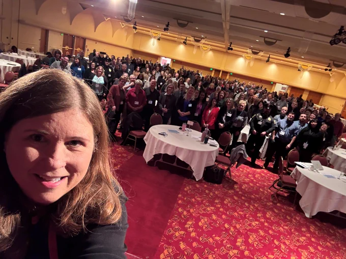 DOA Secretary Kathy Blumenfeld takes a selfie from the stage of the Monona Terrace ballroom with dozens of DOA colleagues on the ballroom floor for the DOA Leadership Conference.