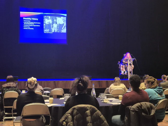 A photo of the VCSE Conference stage. Includes people sitting at tables watching the stage.