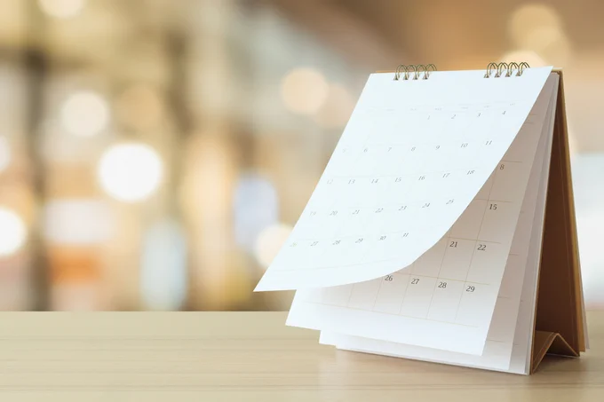 Blurry background with a paper calendar starting to flip up on the edges indicating a looming deadline.