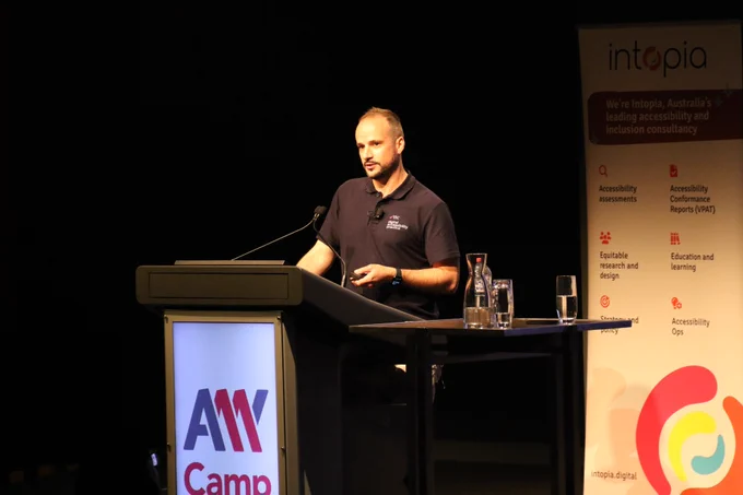 Beau Vass presenting at the A11y Camp lectern, holding a clicker.