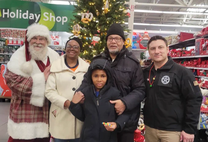 A man dressed as Santa Clause poses with a Deputy U.S. Marshal and Shop with a Cop participants. 
