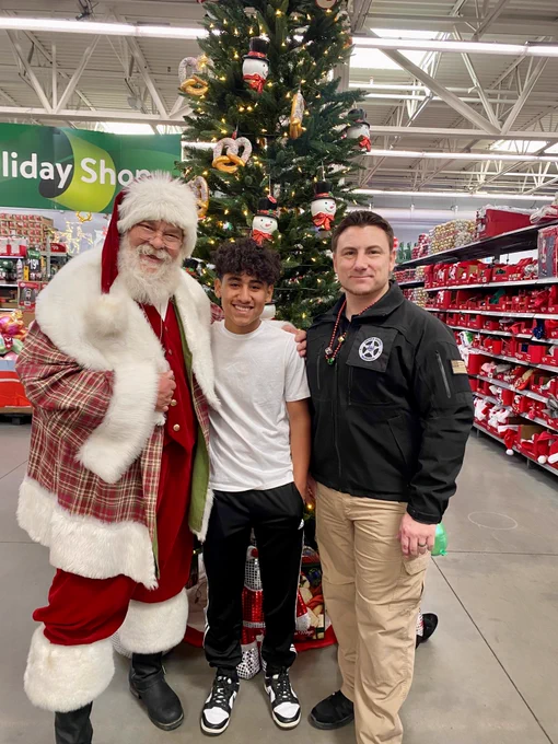 A man is a Santa Clause outfit poses with a youth shopper and a Deputy U.S. Marshal. 