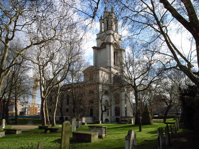Exterior photograph of St Anne's, Limehouse.  Grass and gravestones are in the foreground and trees frame the image. 