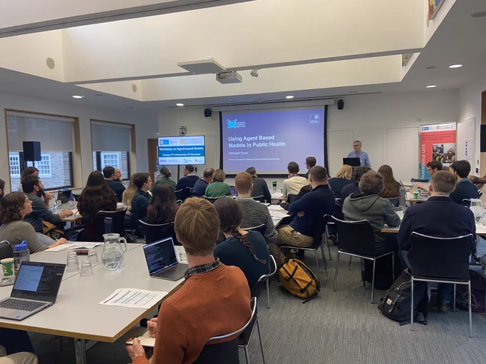 Photo of people sitting and looking at speaker and projector screen.