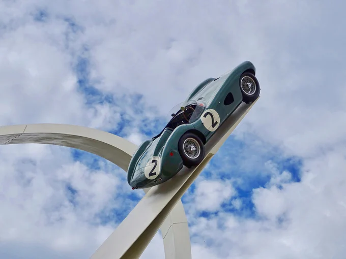 A classical green racing car on a white metal construction, pointing towards a blue sky with plenty of white clouds. The car has number 2 painted in black on white background on the side and trunk. It is probably a piece of art. Photo by Belinda Fewings on Unsplash