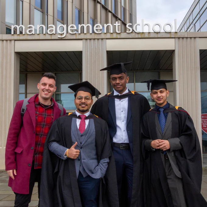 Four graduating students outside the Management School looking towards camera.