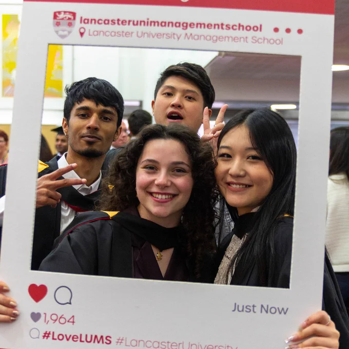 Four graduating students and looking towards camera holding a photo frame.