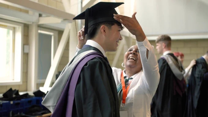 Student getting Graduation cap placed on his head by the gowning team