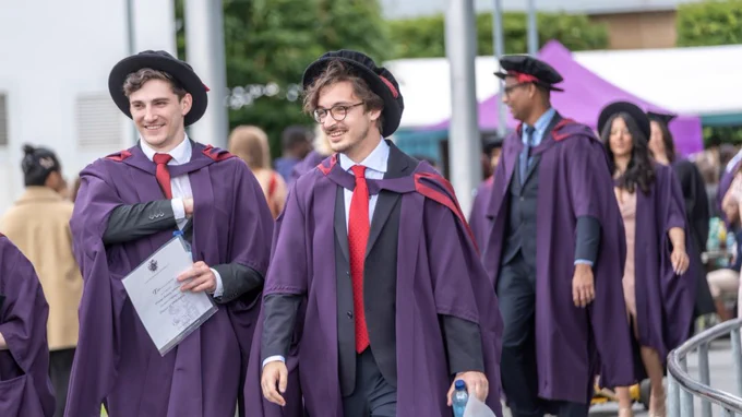 PHD students walking out of graduation hall, smiling to the reception