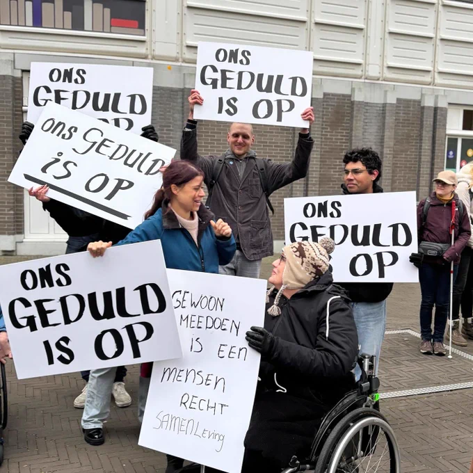Foto buiten bij de Tweede Kamer waar ik samen met verschillende mensen, deels met rolstoel en voetstoots, sta met grote borden “Ons geduld is op” en “gewoon meedoen is een mensenrecht.”
Het is een vrij grijze foto vanwege het weer en de achtergrond.