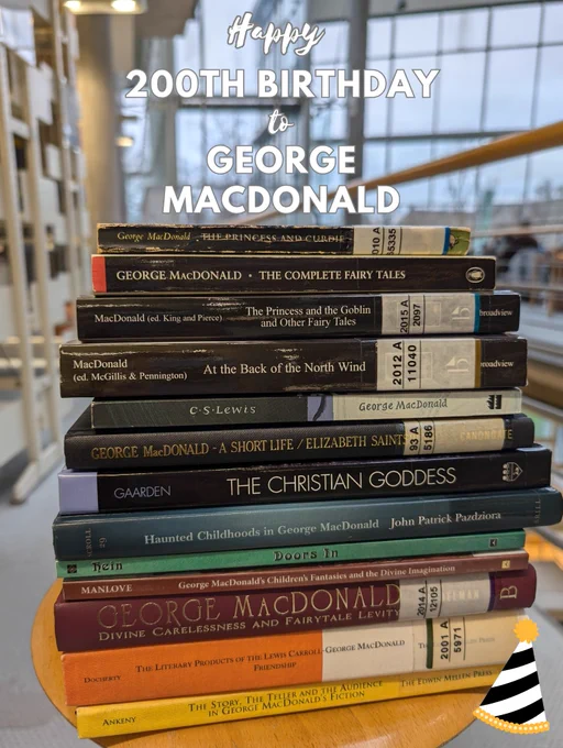 A stack of books by and on George MacDonald in SUB Göttingen, decorated with the image of a birthday hat and the greeting "Happy 200th birthday to George MacDonald" superimposed on the photo
