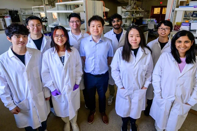 A group of eight laboratory researchers in white coats standing together in a lab setting.