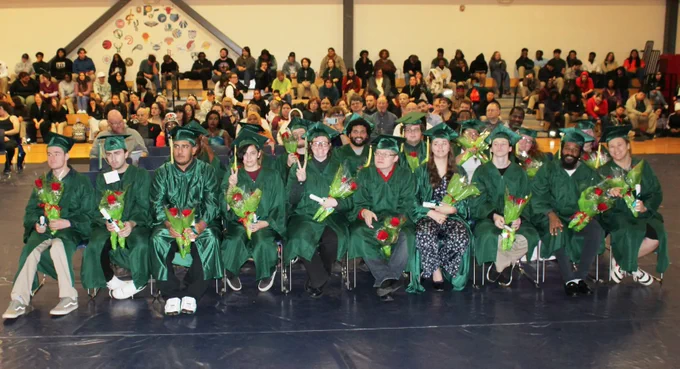 A group of Job Corps graduates sit together in their caps and gowns.