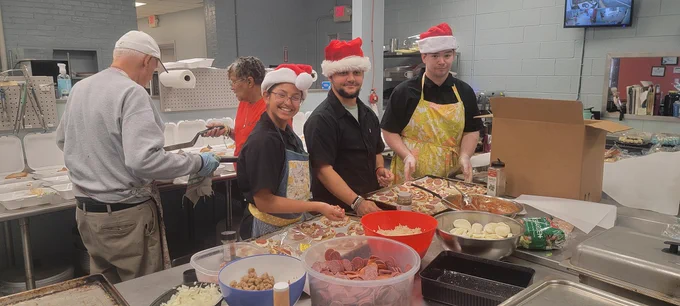 Three people pose for a photo in holiday attire while making snacks.