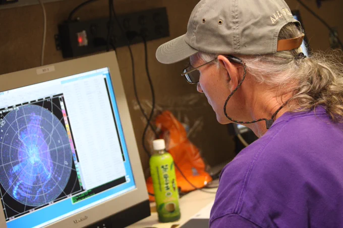 A scientist looking at a screen that is displaying a weather forecast. 