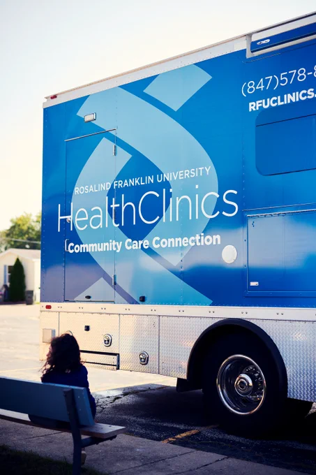 Community member sitting at a bench right outside of the mobile vehicle. The vehicle reads "Rosalind Franklin University HealthClinics Community Care Connection"