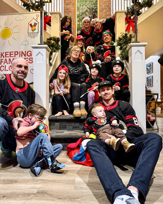 Jake Sanderson, Drake Batherson, Tim Stützle, and Nick Cousins pose for a photo on the stairs with the families at Ronald McDonald House