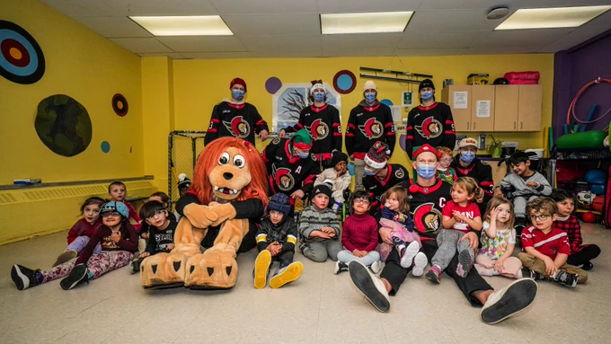 Brady Tkachuk, Thomas Chabot, Adam Gaudette, Michael Amadio, Josh Norris, Nick Jensen, Shane Pinto, Nikolas Matinpalo, and Spartacat pose for a photo with the students at CHEO School