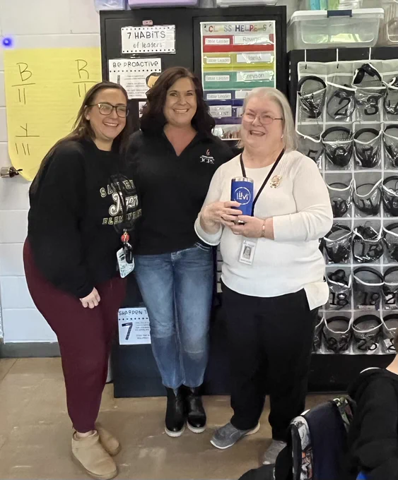 Three people pose for a picture. One holds a mug.