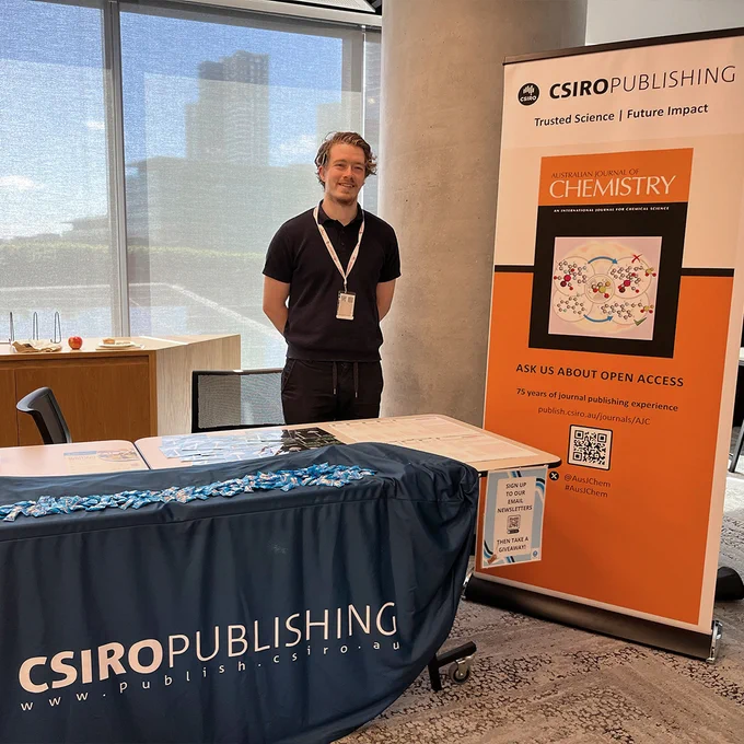 Journal Manager Pat Hannah stands beside an Australian Journal of Chemistry banner at the CSIRO Publishing stand.