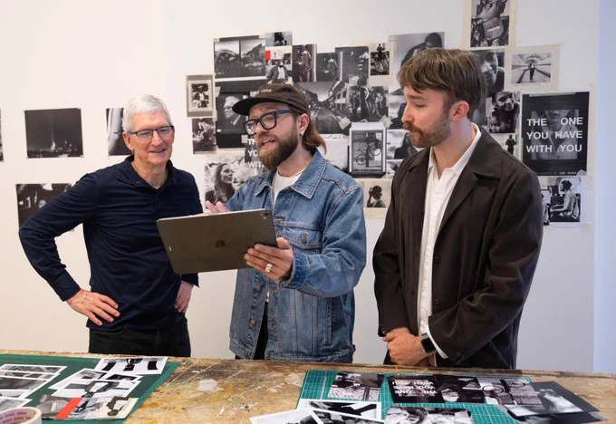 Tim stands beside Will and Ed. Will holds iPad Pro and shows Tim their work. Pages from the Reid's book are taped to the white wall behind them