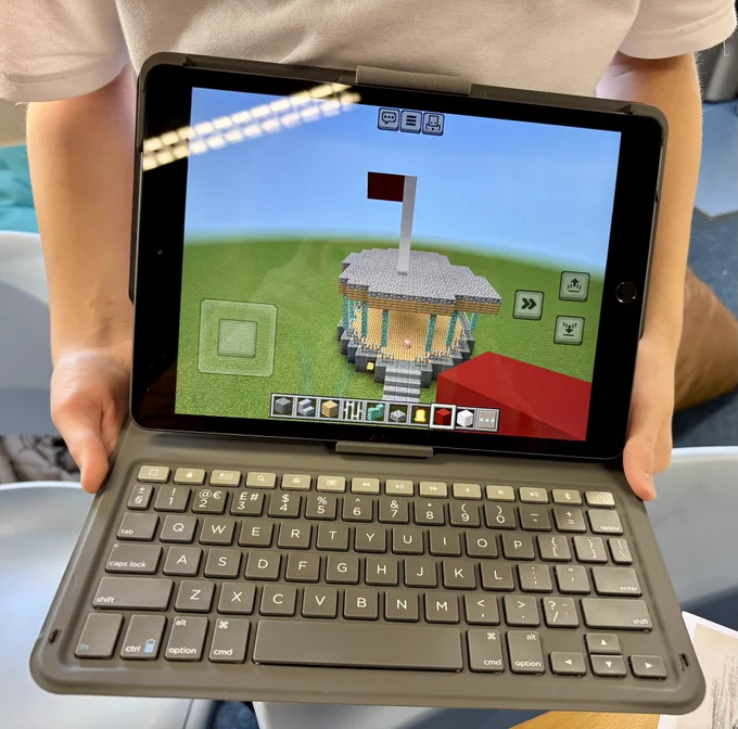 Photo of a young person holding a small laptop. On the screen is a bandstand created in Minecraft.