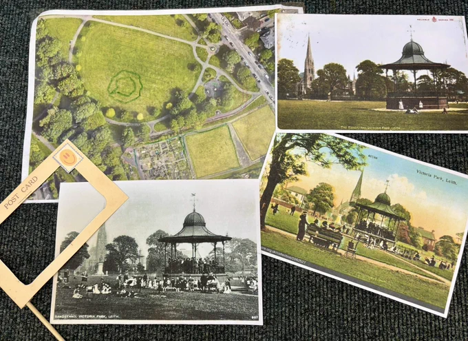 Photo showing three historic postcards featuring the bandstand in Victoria Park, a modern aerial photo of the park and a cut out postcard ‘view finder’ on a stick.
