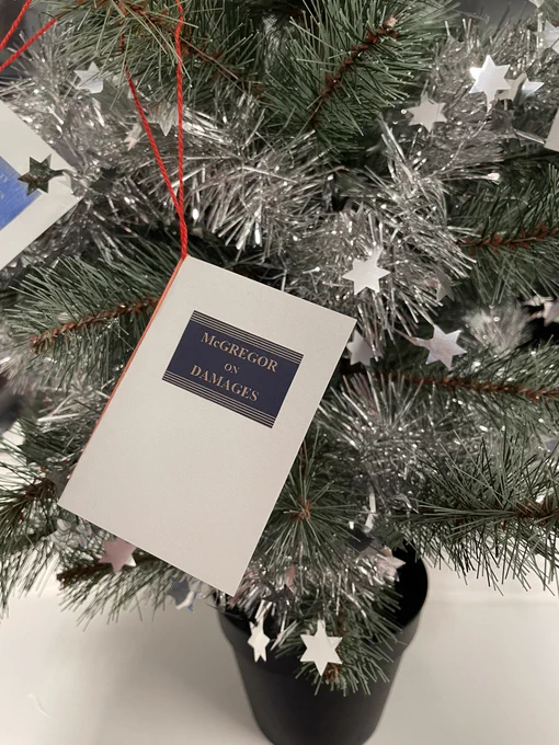 Christmas tree decoration in the shape of a small version of the book McGregor on Damages. The decoration is on a small artificial tree with silver tinsel.