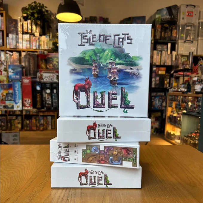 Several copies of the board game the Isle of Cats Duel stacked on top of each other in the board game shop Ancient Robot Games. Games and plants can be seen in the background.
