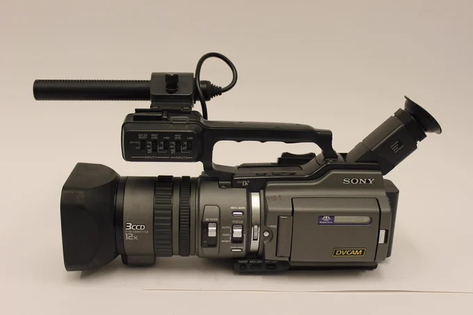 The side profile of a Sony DSR-PD150p DVCAM. This camera is a big one, the type used for broadcasting TV. It has a microphone attached on top and a big lense.