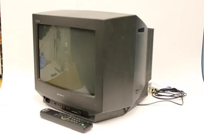 A Sony Triniton TV KV-14TIU television. It is a grey colour and has a little remote in front of it. There is a wire attached to it.