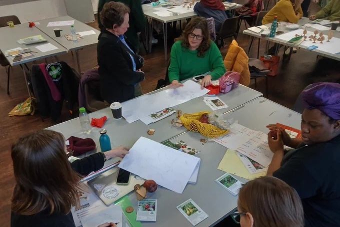 A group of women sit around a table filled with papers, designs, and fruit tree information.