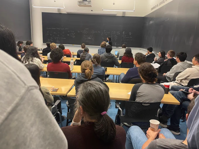 Full-color image of a packed classroom at Frick Lab, with the speaker upfront at chalkboard.