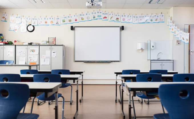 School classrom with whiteboard and blue chairs at rows of desks
