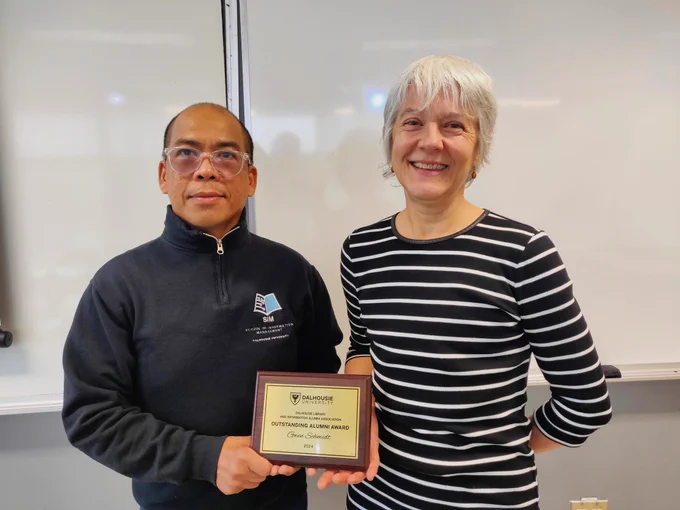 Gwen poses for a photo next to fellow alum Mark, who is holding a gold plaque. 