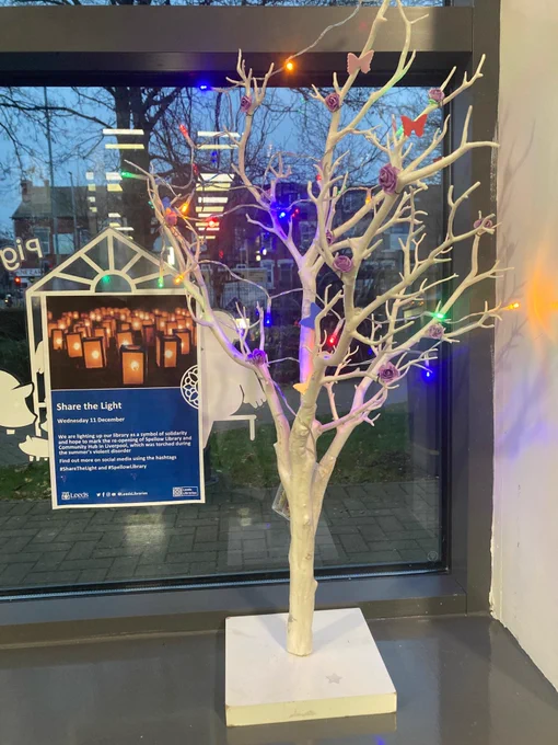 A white tree in a window with fairy lights in it