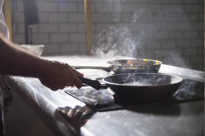 Close-up of someone cooking with two sizzling pans on a hob.
