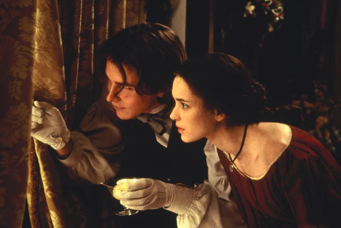 Two figures peer out a window to the left of the image, peeling back the curtain. The actors are Christian Bale and Winona Ryder.