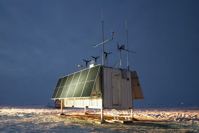 Solar panel is folded downward, a light glowing from it towards a snowy ground beneath. The sky is dim blue, with minimal light along a snowy horizon. 