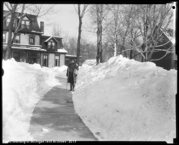 Woman with snowshoes on a cleared sidewalk in front of a large house