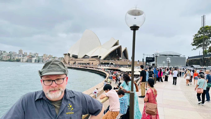 Picture of Rick wearing his green hat standing in a crowd with a Australian Opera House in Sydney in the background. He’s confused as to what time zone he’s in.