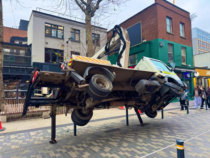 A truck is left balancing on its side on bollards. All wheels off the ground.