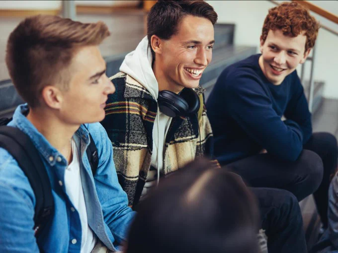 Three friends sitting and laughing together, one wearing headphones around their neck.