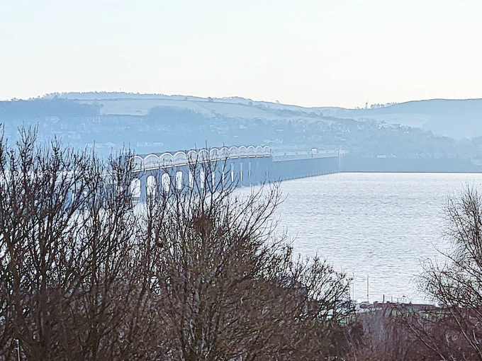 View of a rail bridge across the river Tay with the Fife country side in the distance 