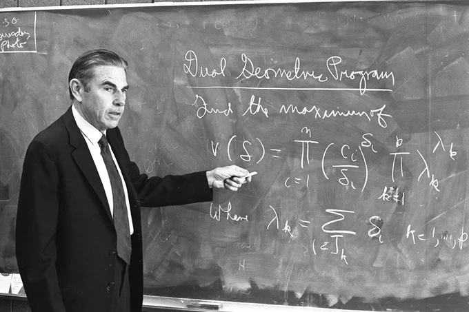 Mathematician Richard Duffin stands in front of a chalkboard and gestures at an equation.