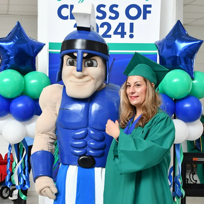 Mr. Titan mascot and female graduate in green cap and gown with green, blue and white balloons