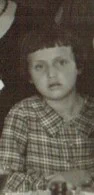 Vintage black and white photo of a young girl with a subdued expression, wearing a plaid shirt.