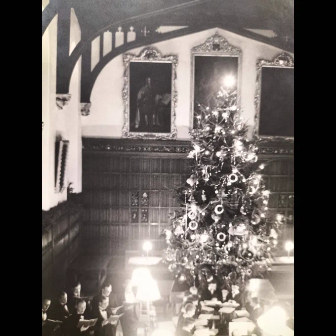 Black & white photograph of choir singing in the College Hall under a very large Christmas tree, dating from the 1950s. Archive reference: P424/P1/2 
