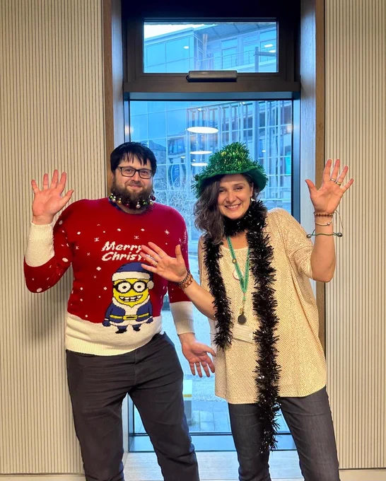 Image shows 2 library staff with festive and sparkling jumpers, hats and beard baubles